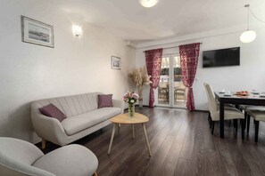 A living room with a sofa, a small round table with a vase, a dining table with chairs, and a TV mounted on the wall. - Holiday apartment near Pical Beach (Poreč)