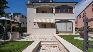 A two-story house with a stone pathway leading to the entrance, a covered patio, and a well-maintained lawn. - Holiday apartment near Pical Beach (Poreč)