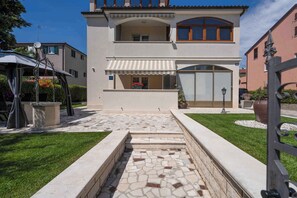 A two-story house with a stone pathway leading to the entrance, a covered patio, and a well-maintained lawn. - Holiday apartment near Pical Beach (Poreč)