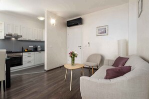 A modern living space with a kitchen, a sofa, a chair, and a small table with a vase. - Holiday apartment near Pical Beach (Poreč)