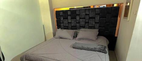 Un dormitorio con cama, cabecera, equipo de aire acondicionado y lámpara en el techo.