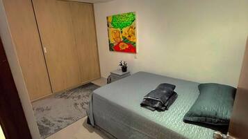 Et soveværelse med seng, garderobe, natbord, et maleri og en loftlampe.