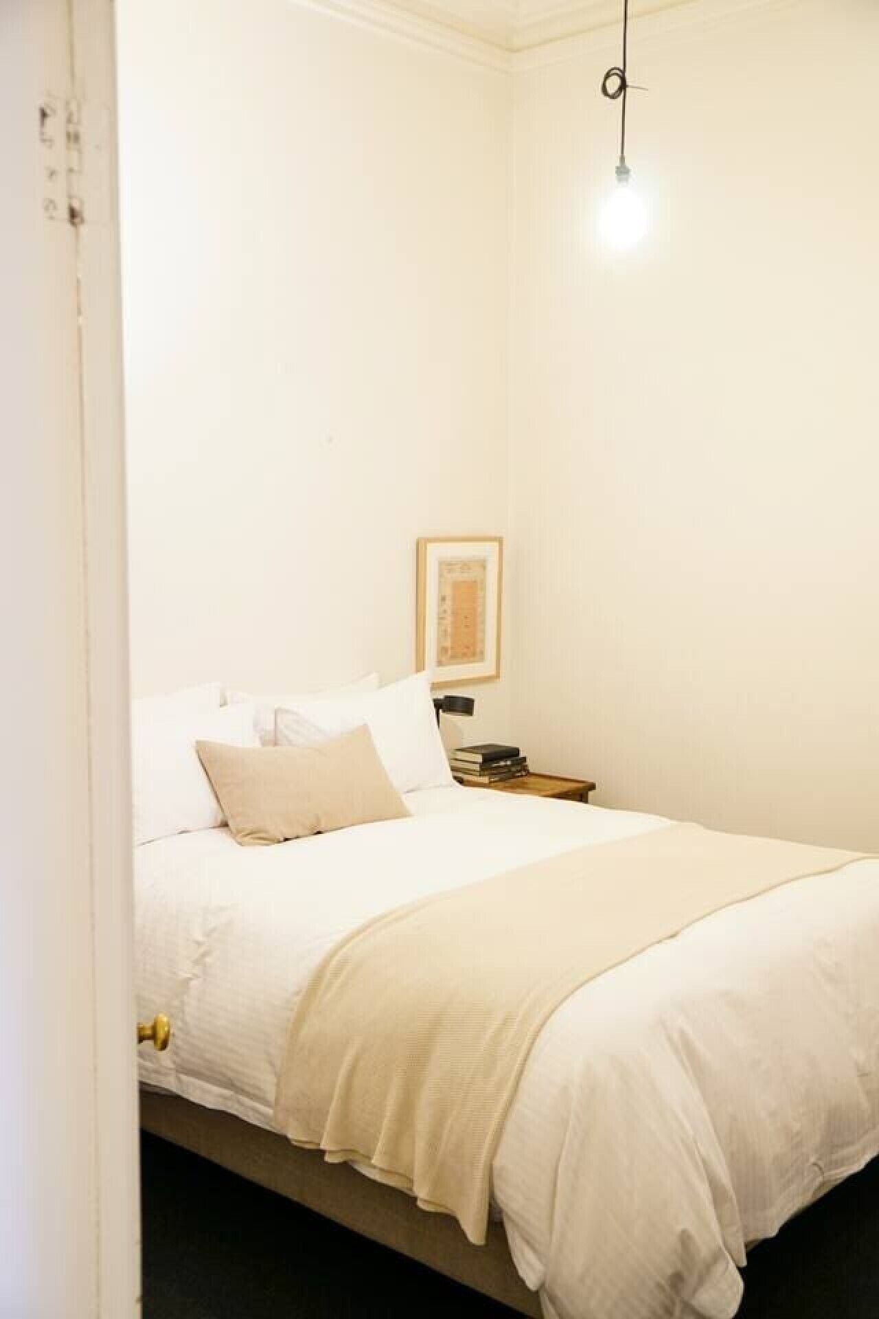 A bedroom with a bed, a bedside table, a lamp, and a hanging light fixture.