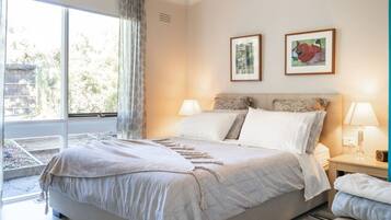 A bedroom with a large bed, two bedside lamps, a window with curtains, and two framed pictures on the wall.