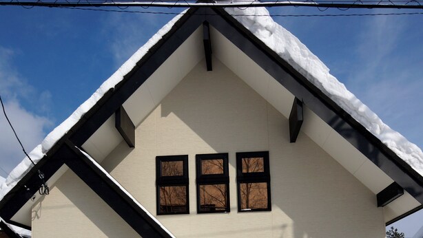 Una casa de dos pisos con techo nevado y puerta negra.