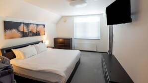 Una habitación de hotel con cama, televisor de pantalla plana, ventana, radiador y un cuadro en la pared.
