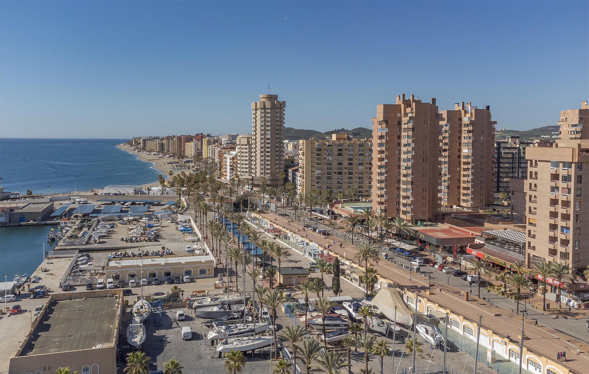A coastal cityscape with high-rise buildings, a marina, and a beach.