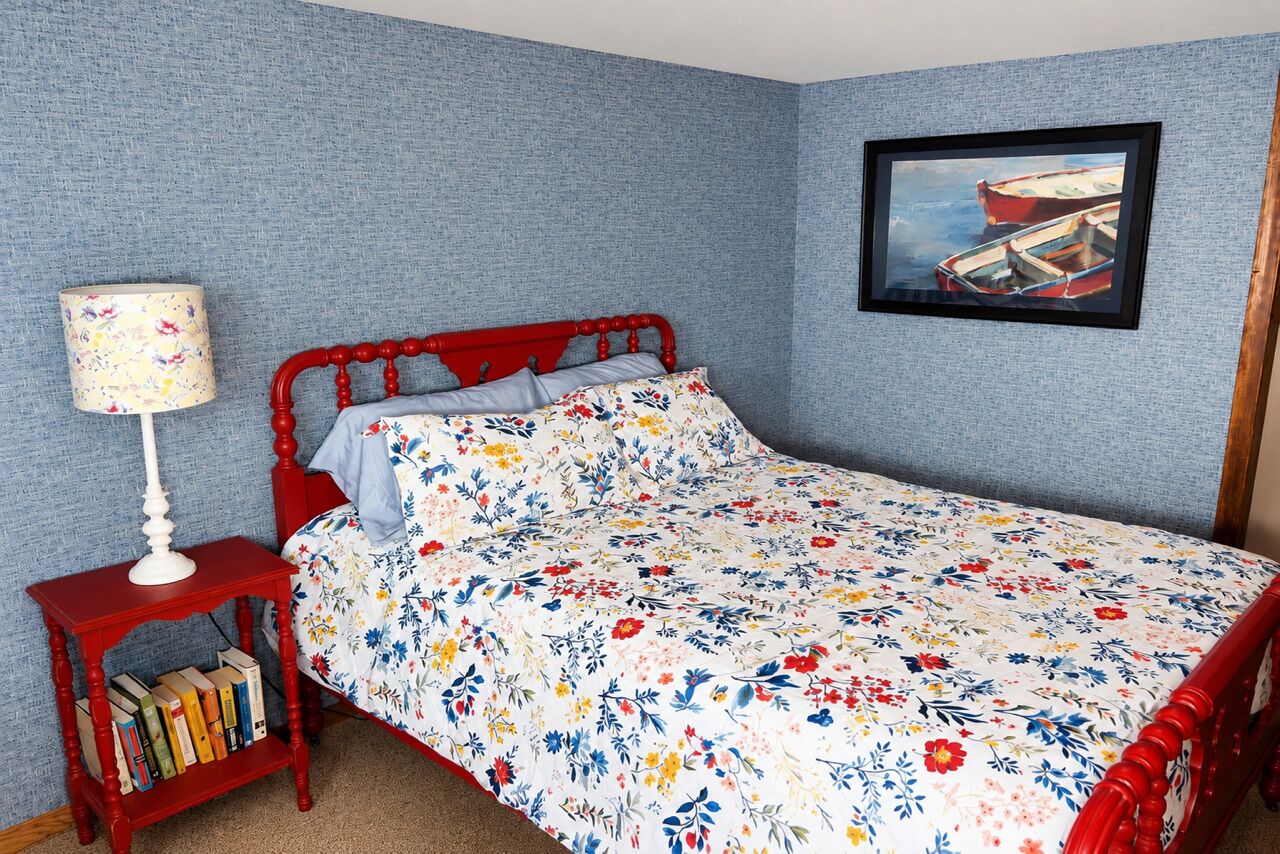 A bedroom with a bed, a nightstand with books, a lamp, and a painting on the wall.