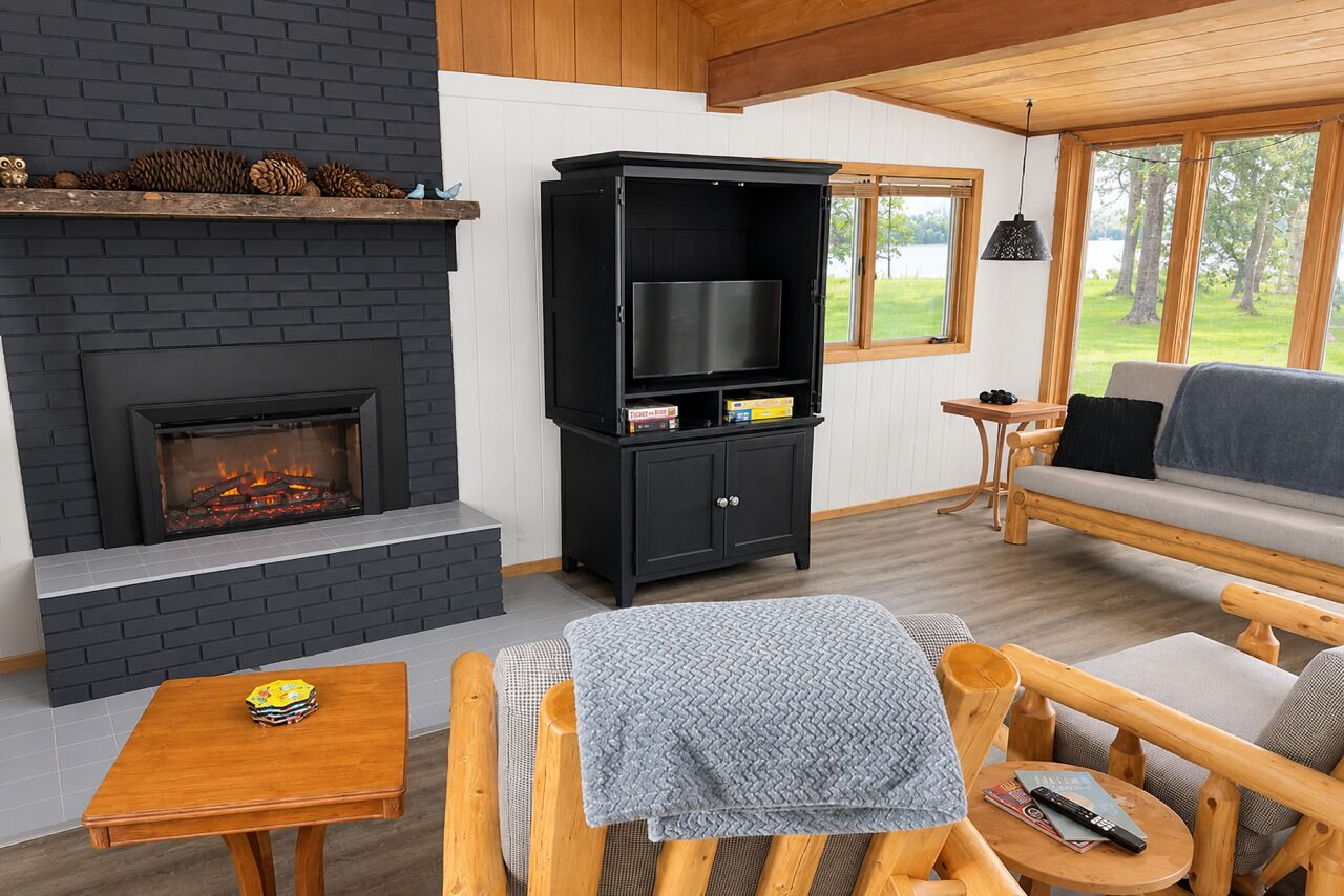 Una sala acogedora con chimenea, un mueble de entretenimiento negro, muebles de madera y vistas al exterior.