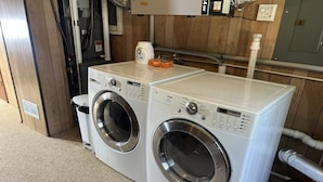 A laundry area with two front-loading washing machines and a trash can.