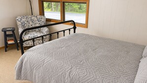 A bedroom with a bed, a chair, a small stool, and a window.