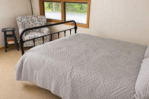 A bedroom with a bed, a chair, a small stool, and a window.