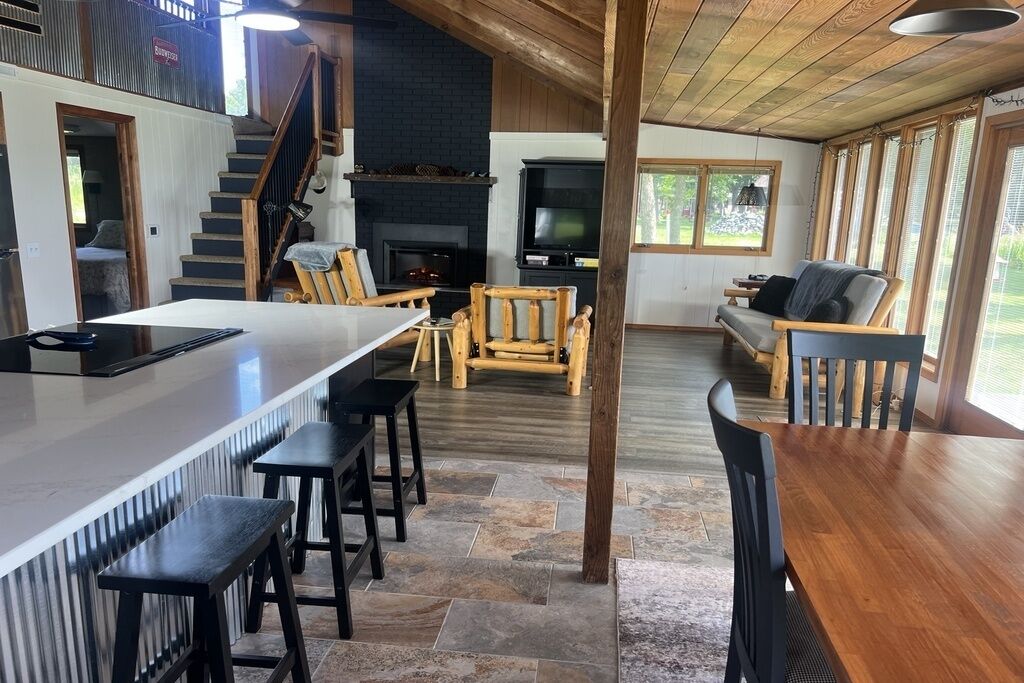 A modern kitchen with a large island, wooden chairs, and a fireplace.
