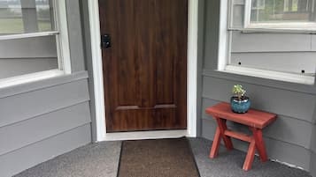 Una puerta de madera con un panel de vidrio, un banco rojo y un felpudo frente a una casa.