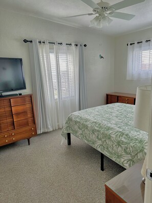 A bedroom with a bed, a TV on a dresser, a ceiling fan, and a window with curtains. - Charming Mid Century Modern Home w/office and large outdoor space (St. Petersburg)