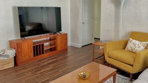 Ein Wohnzimmer mit Fernseher, Holz-Unterhaltungseinheit, Sofa, Couchtisch und einem gemusterten Teppich.