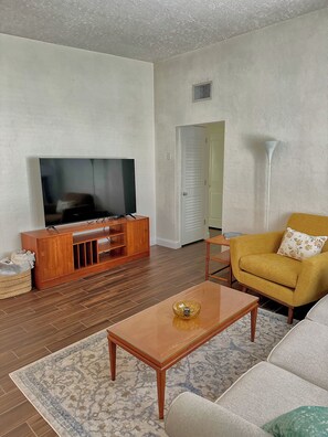 A living room with a television, wooden entertainment unit, sofa, coffee table, and patterned rug. - Charming Mid Century Modern Home w/office and large outdoor space (St. Petersburg)