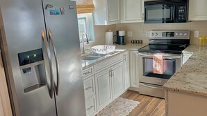 Eine Küche mit weißen Schränken, Edelstahlgeräten, einer Mikrowelle, einem Backofen und einem Kühlschrank.