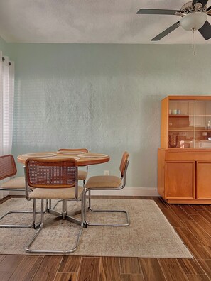 A dining area with a round table, four chairs, a ceiling fan, and a wooden cabinet. - Charming Mid Century Modern Home w/office and large outdoor space (St. Petersburg)