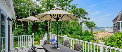 A deck with wicker furniture and a table, surrounded by white railings, overlooking a beach.