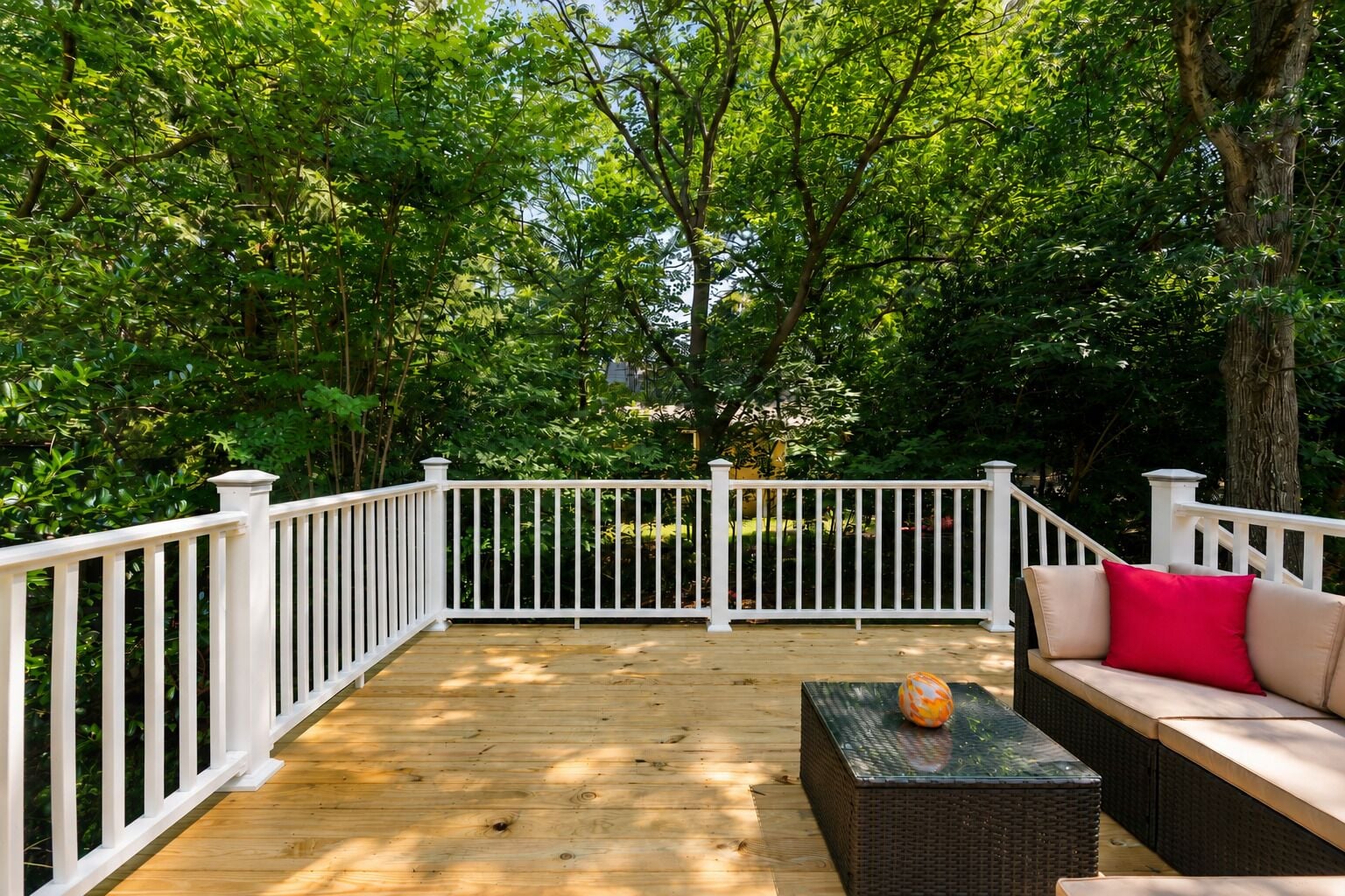 A wooden deck with white railings, surrounded by lush greenery.