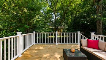 A wooden deck with white railings, surrounded by lush greenery.