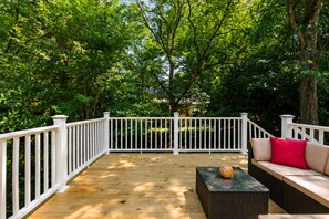 A wooden deck with white railings, surrounded by lush greenery.