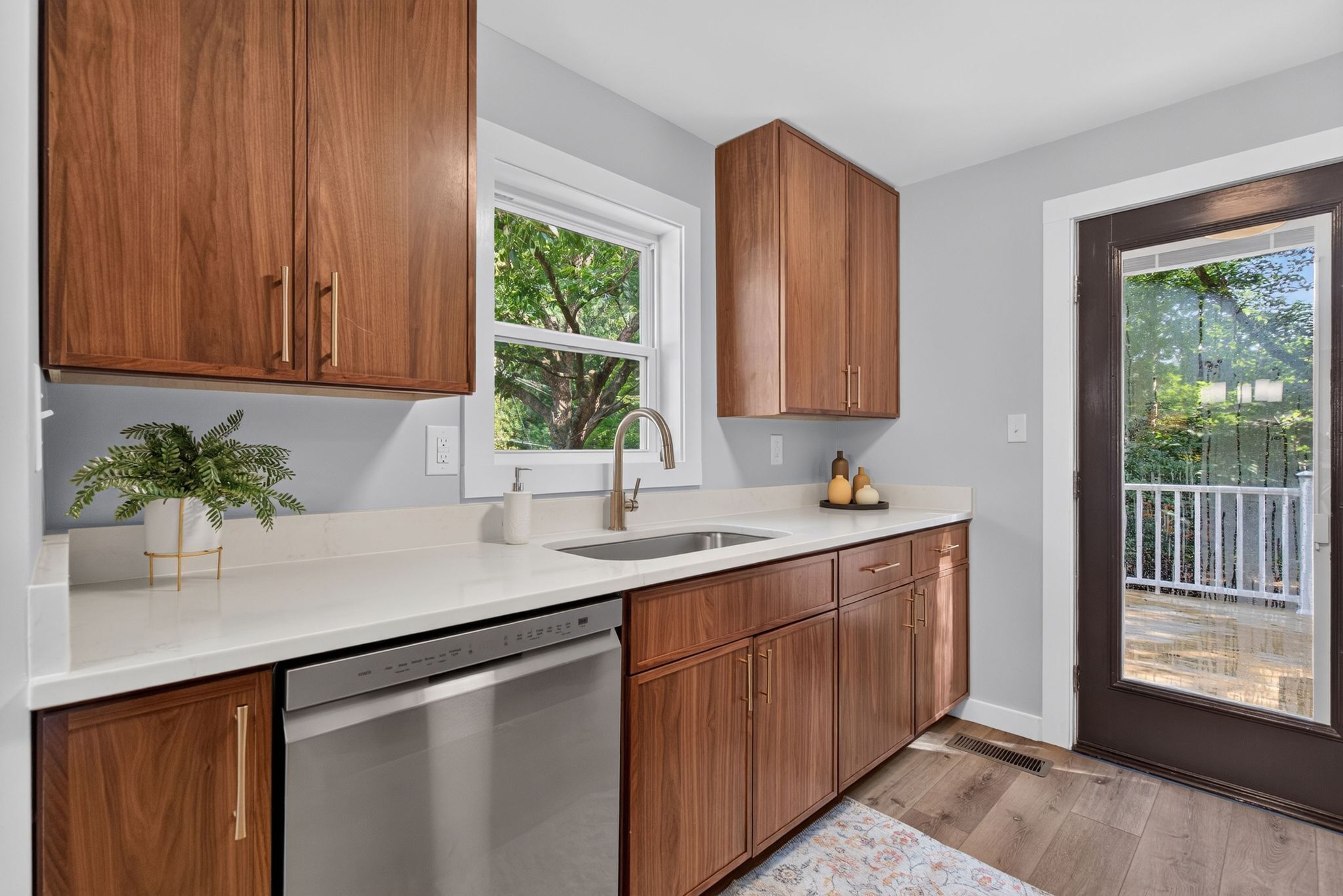 A kitchen with wooden cabinets, a white countertop, a dishwasher, and a window with a view of trees.
