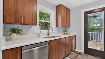 A kitchen with wooden cabinets, a white countertop, a dishwasher, and a window with a view of trees.