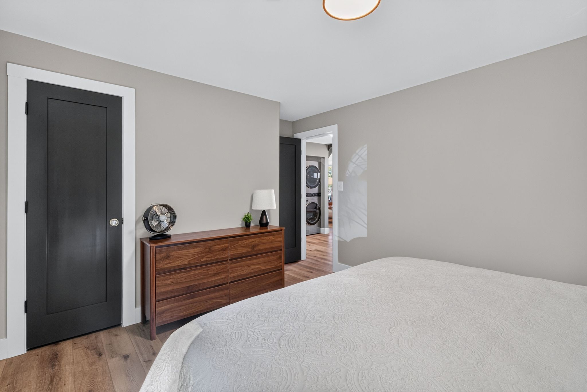 Un dormitorio con cama, cómoda, puerta y zona de lavandería visible a través de una puerta abierta.