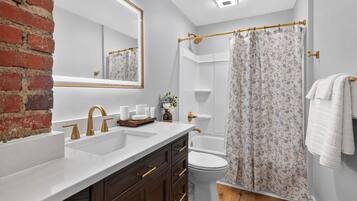A bathroom with a white sink, gold faucets, a wooden vanity, a toilet, and a shower curtain.