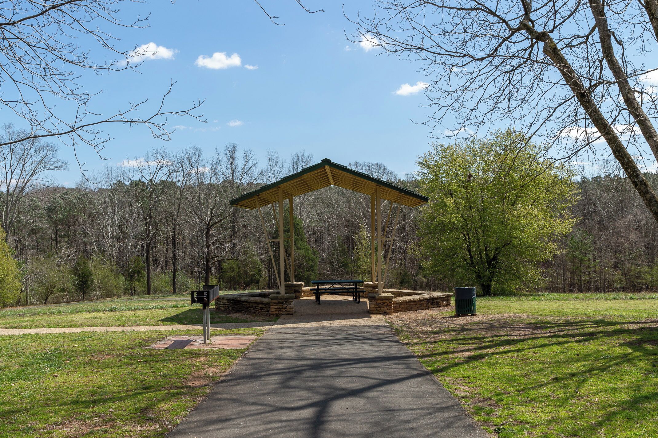 A park with a wooden pavilion, a picnic table, and a trash can.
