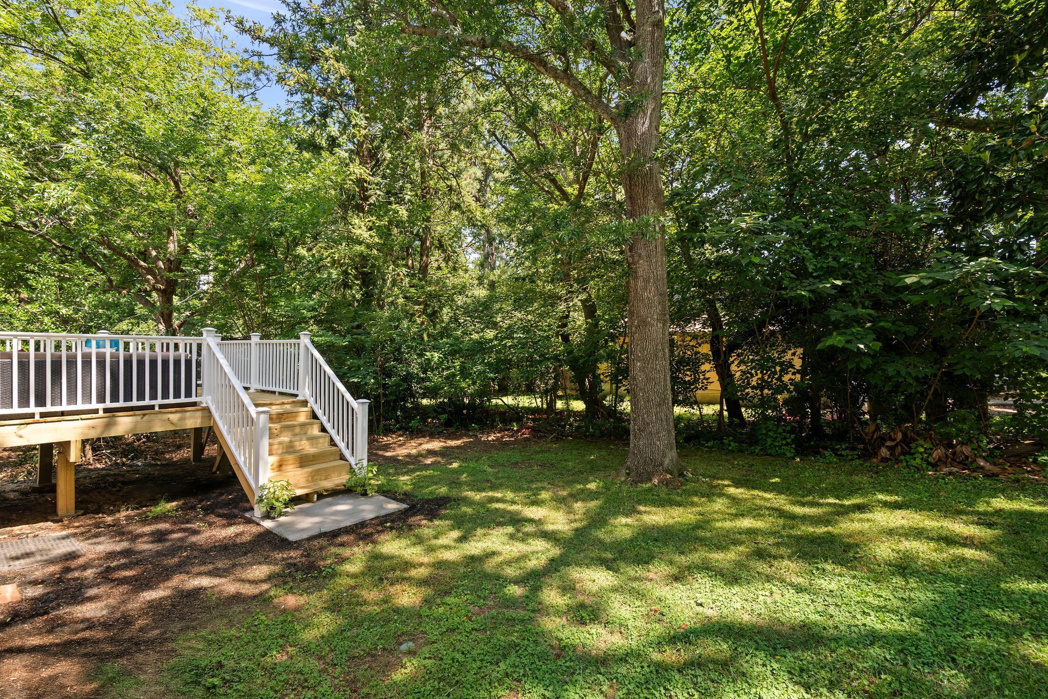A wooden deck with a white railing leading to a grassy area surrounded by trees.