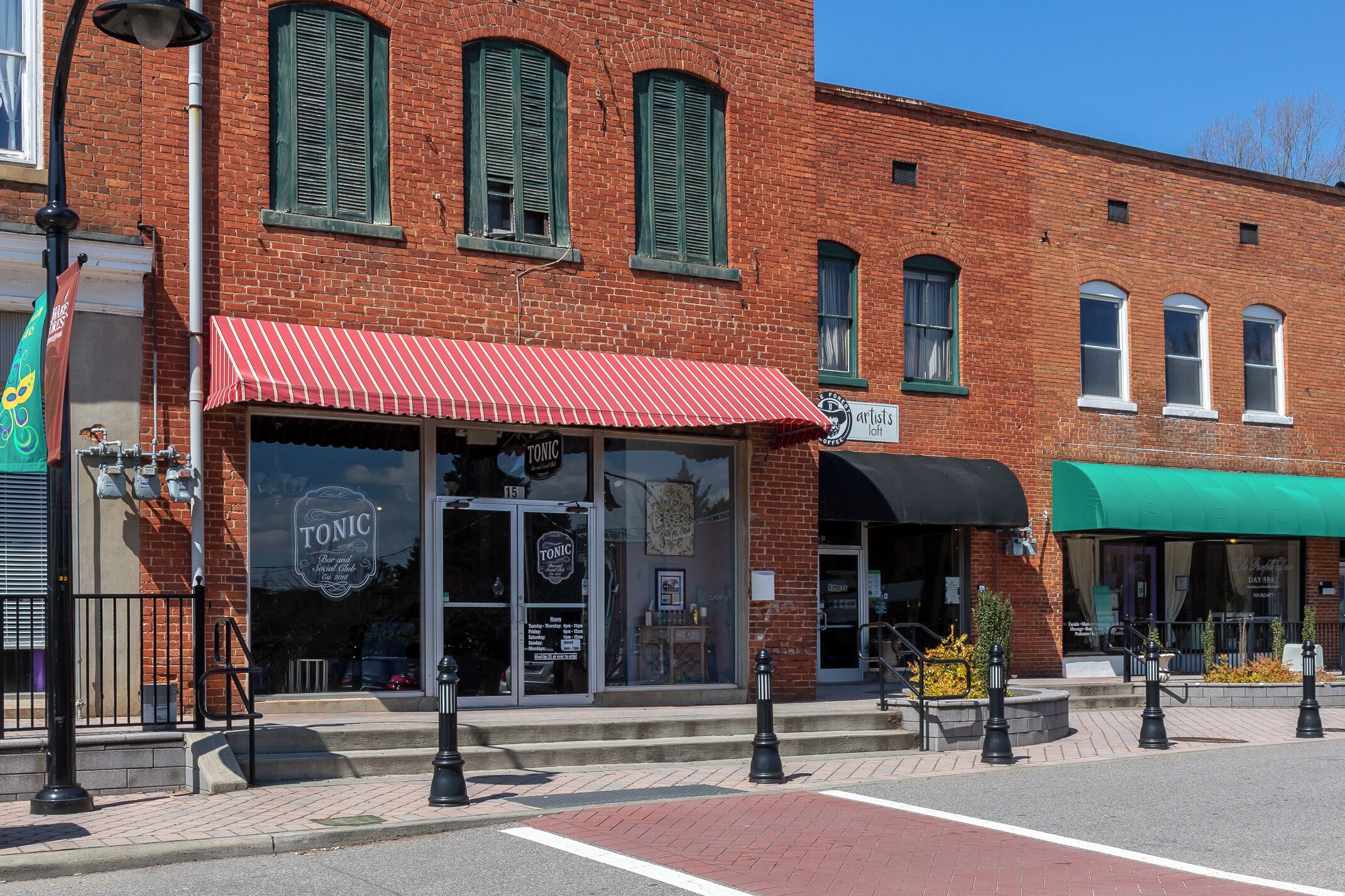 A brick building with a red awning, a storefront with a sign reading 'TONIC Bar and Social Club,' and a green awning to the right.
