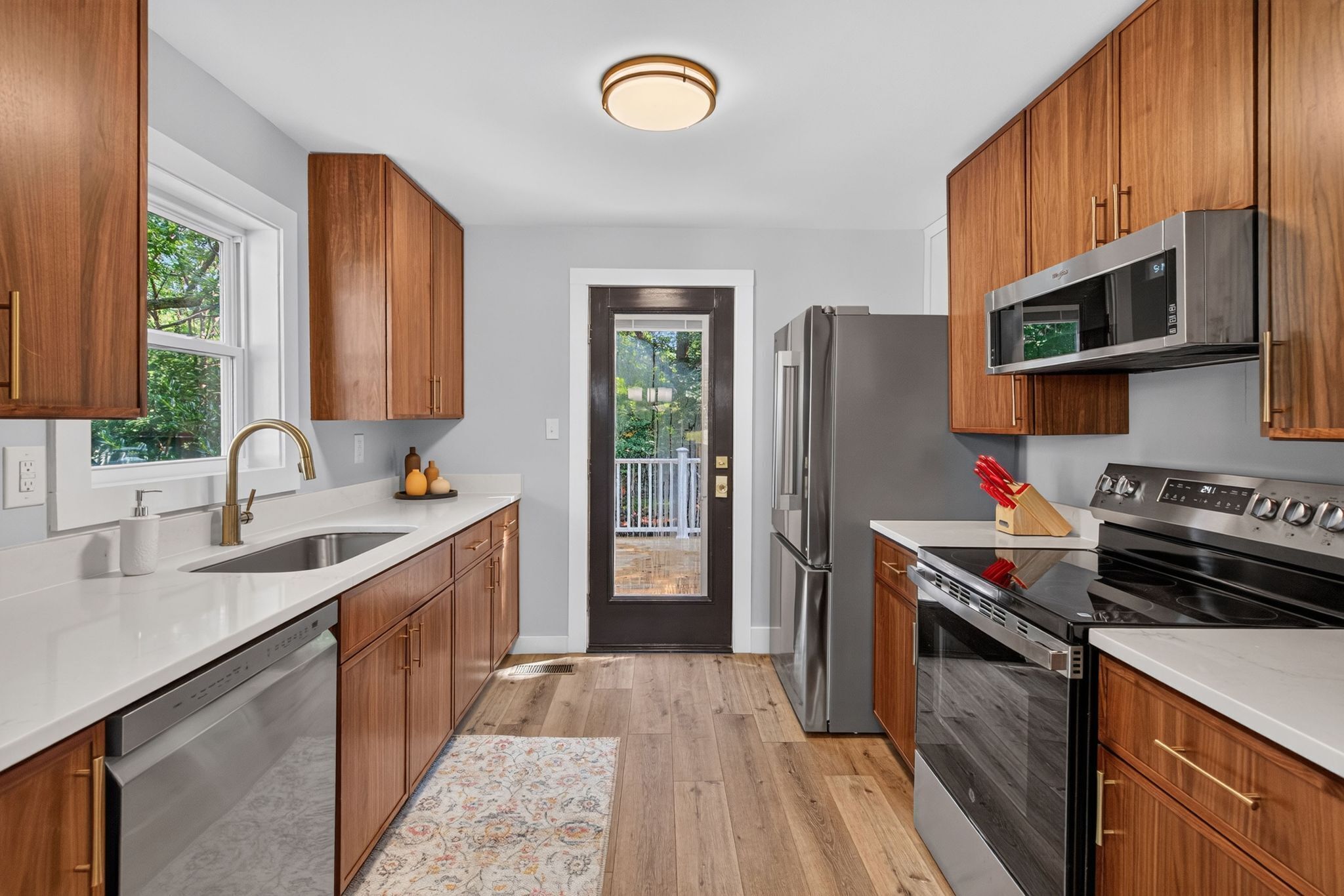 A modern kitchen with wooden cabinets, stainless steel appliances, and a view to the outside.