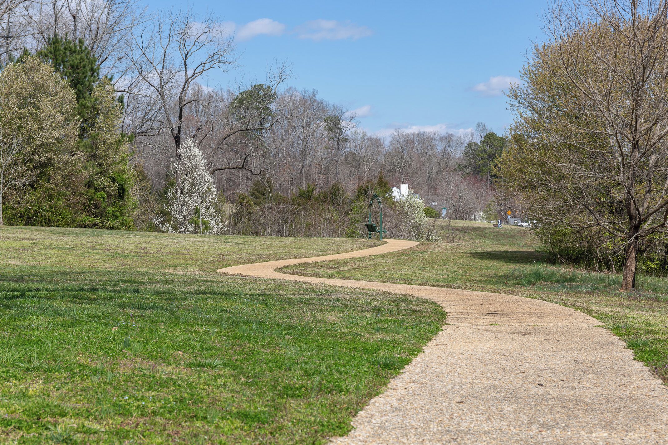 A gravel path winding through a grassy park with trees and a white building in the distance.