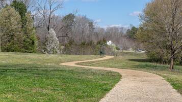 A gravel path winding through a grassy park with trees and a white building in the distance.