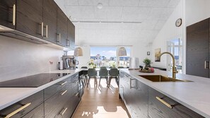 A modern kitchen with a central island, dark wood cabinets, and a large window offering a view. - VillaVilla 959 - Nr. Lyngby ved Løkken, nordjyllan (Løkken)