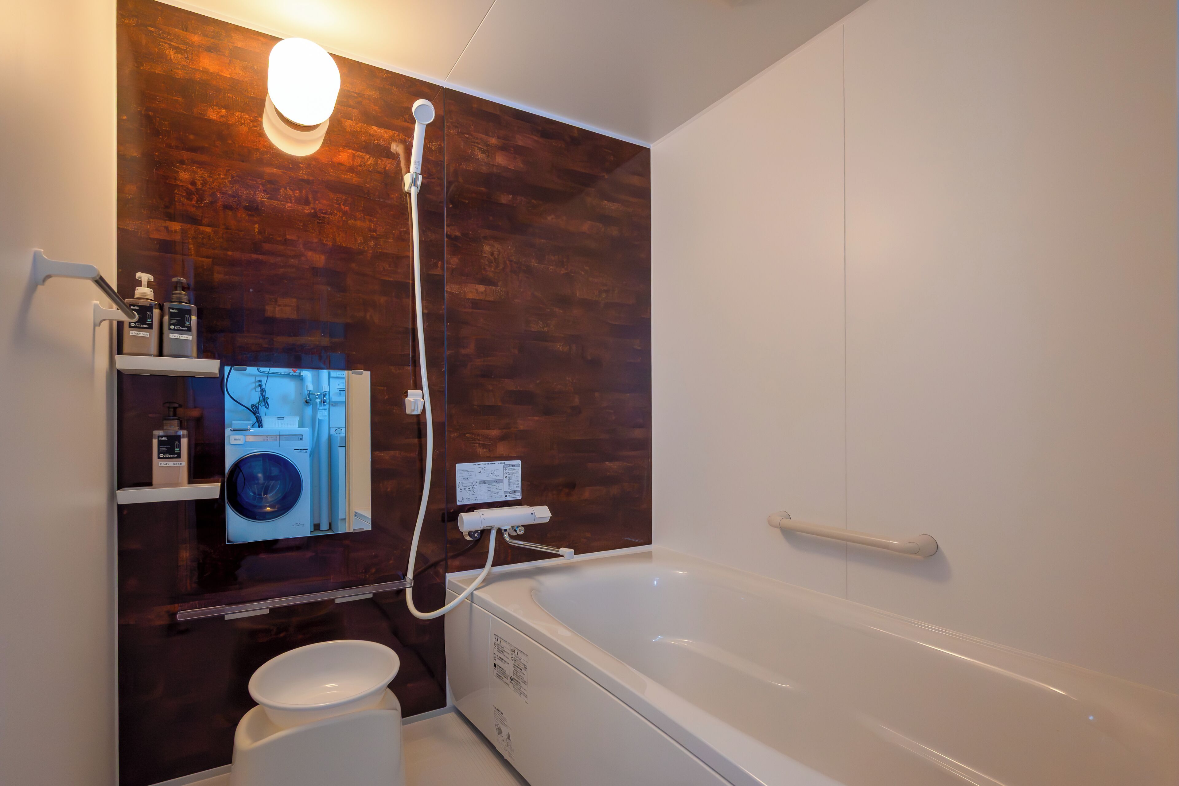 A modern bathroom with a wooden accent wall, a built-in washing machine, and a large bathtub.