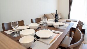 A dining table set with white plates, bowls, cutlery, and a wine glass, with a sofa and curtains in the background. - North Point Kamifurano (Sorachi-gun,Kamifurano-cho)
