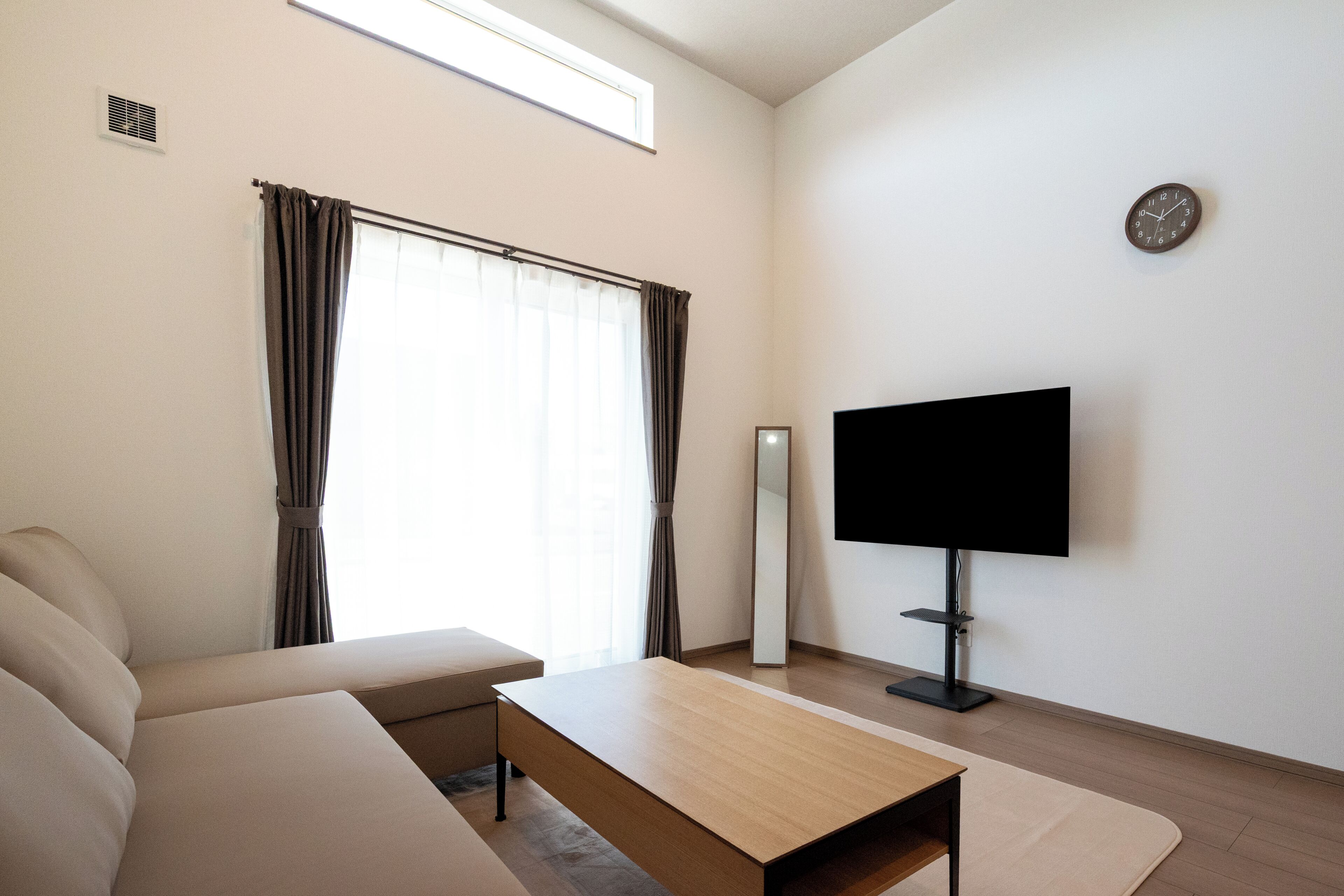 A modern living room with a sofa, a coffee table, a flat-screen TV, and a large window with curtains.