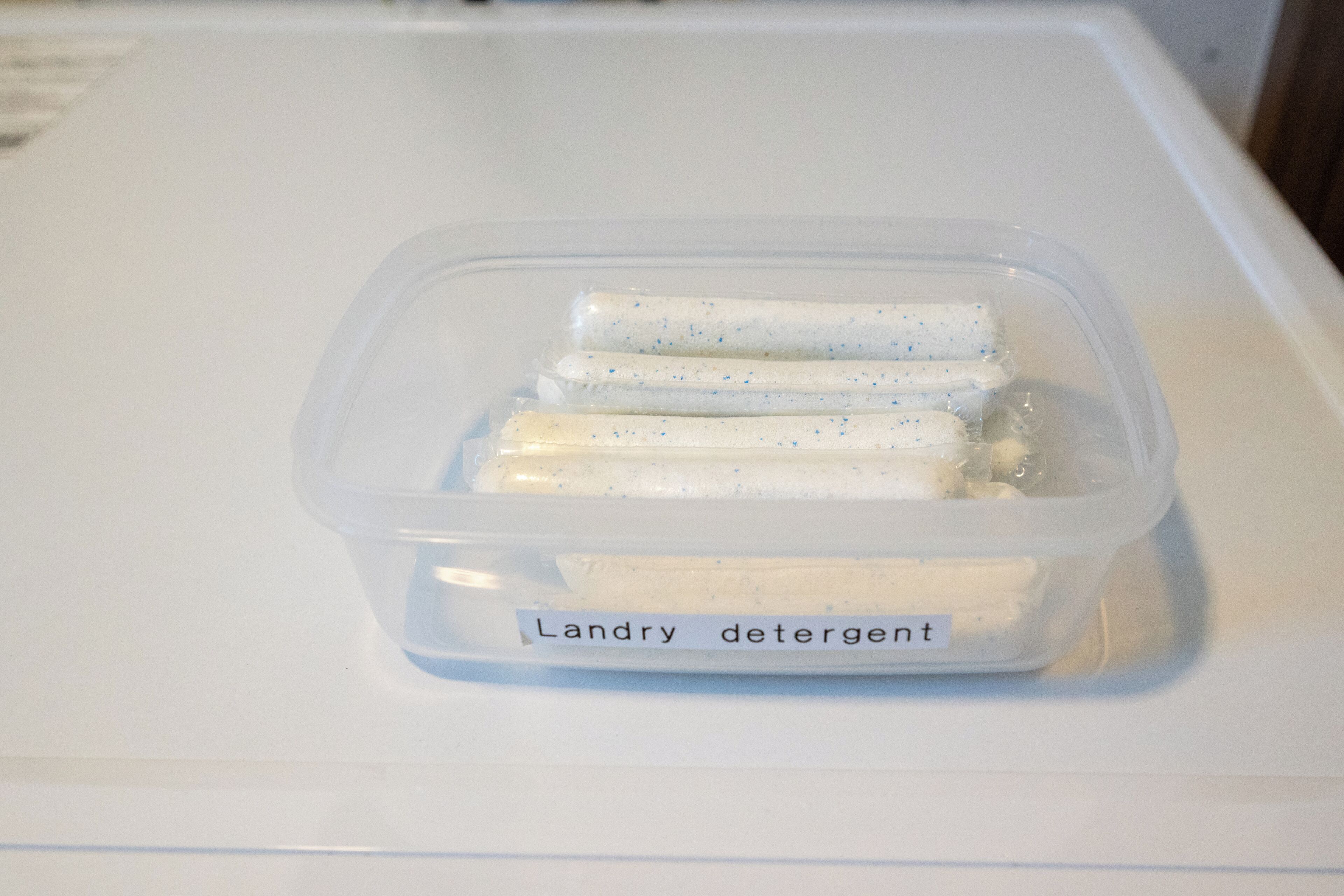 Un récipient en plastique portant l’étiquette « Détergent à lessive », posé sur une surface blanche.