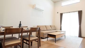 A modern living room with a sofa, dining table, chairs, and a large window with curtains.