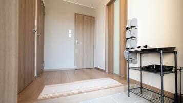 A hallway with wooden flooring, a white door, a metal rack with shoes, and a tiled floor.