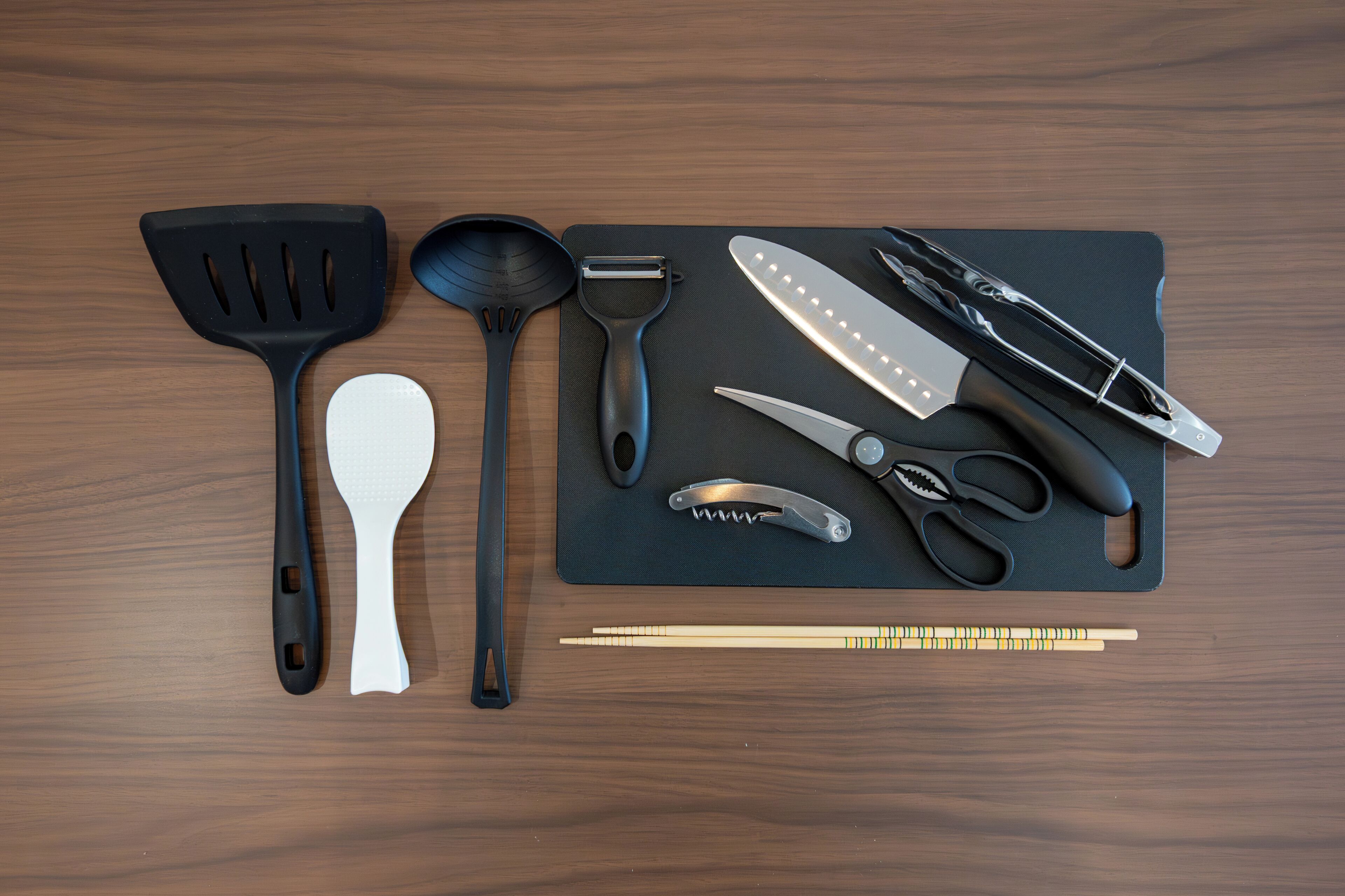 A set of kitchen utensils and tools laid out on a dark mat.
