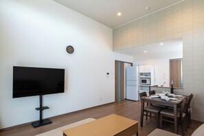 Una sala moderna con televisor de pantalla plana, una mesa de comedor lista para cuatro personas y una cocina al fondo.