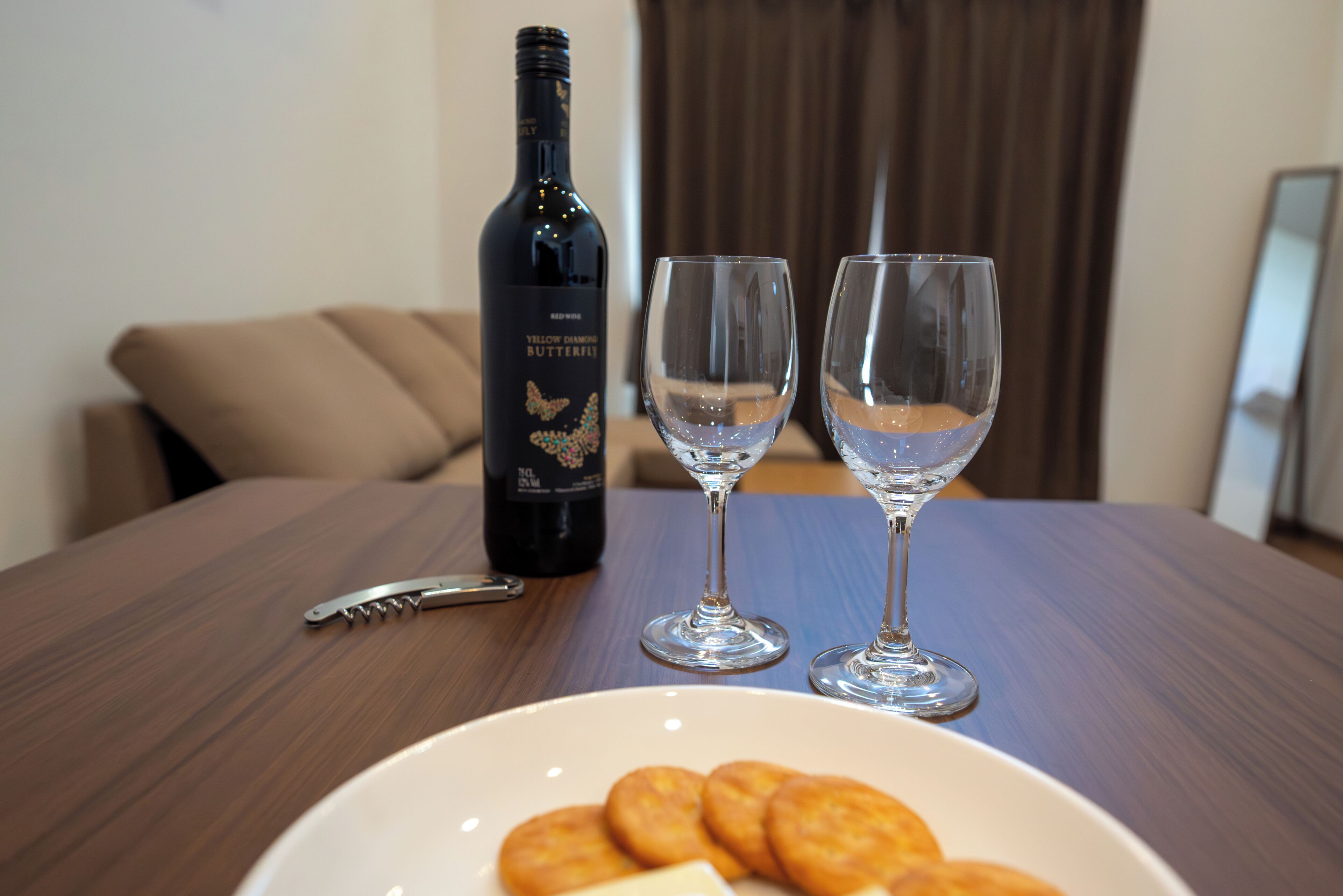 A bottle of wine, two glasses, and a plate with biscuits on a wooden table.