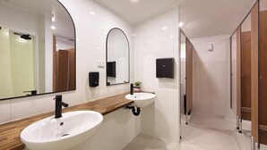 A modern bathroom with two sinks, a large mirror, and a shower area. - Herveys (Pialba)