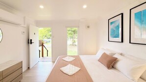 A hotel room with a bed, a wooden dresser, and a view of the outdoors. - Herveys (Pialba)