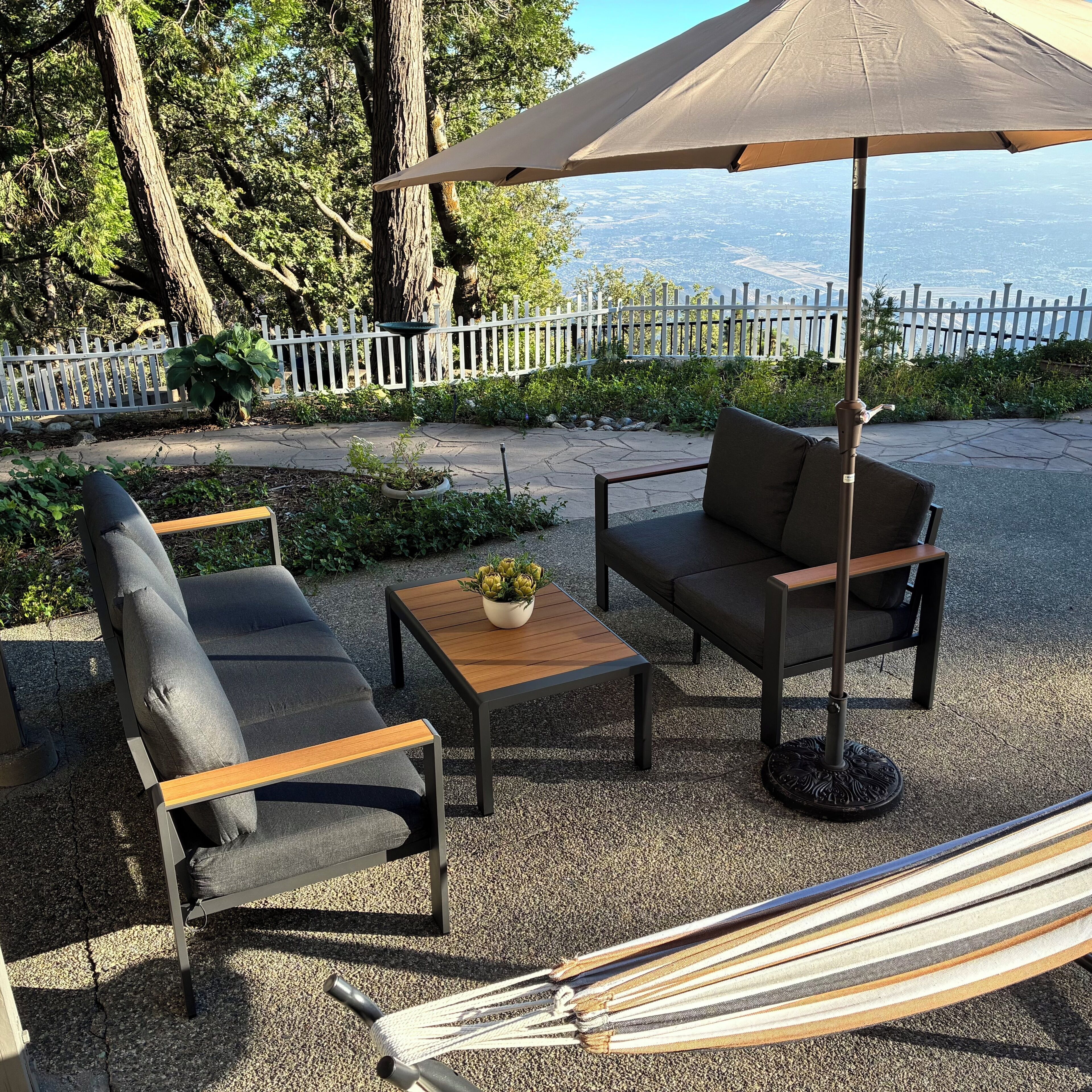Een buitenzitplaats met een hangmat, twee stoelen, een tafel en een grote parasol.